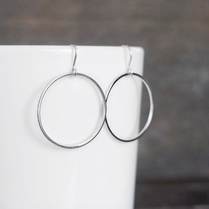 May include: A pair of silver hoop earrings with a simple, circular design. The earrings are made of a thin, smooth metal and have a polished finish.