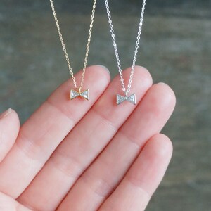 May include: Two delicate necklaces, one in gold-tone metal and one in silver-tone metal, each featuring a small, clear, triangular-shaped crystal pendant arranged to form a bow shape suspended from a thin, matching link chain.