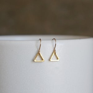 May include: A pair of gold triangle earrings with a simple, minimalist design. The earrings are small and delicate, perfect for everyday wear.