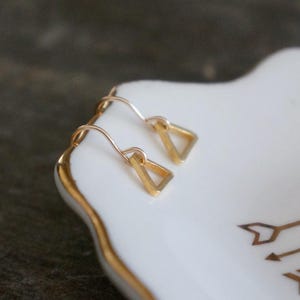 May include: A pair of gold triangle earrings with a simple design. The earrings are small and delicate, and they would be a great addition to any jewelry collection.