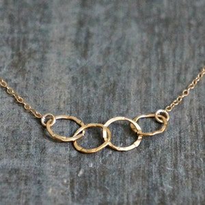 May include: A gold necklace with a delicate chain and a pendant made of four interlocking circles. The circles are hammered and have a textured finish.