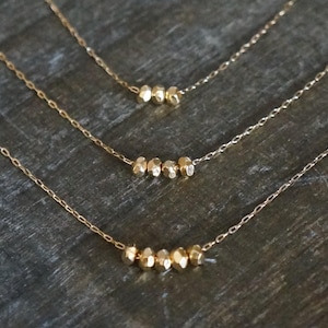 May include: Three gold necklaces with varying lengths, each featuring a row of small, irregular gold beads.