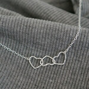May include: A silver necklace with three interlocking heart charms. The hearts are made of a delicate, twisted wire.