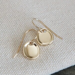 May include: A pair of gold-toned earrings with a simple, round disc design. The earrings are made of a smooth, shiny metal and have a delicate, minimalist style.