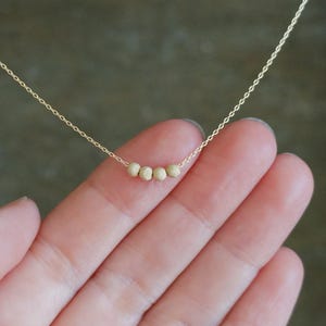 May include: A delicate gold necklace featuring five small, textured beads. The beads are evenly spaced along a fine gold chain. The necklace is displayed against a soft, neutral background, highlighting the jewelry's simple elegance.
