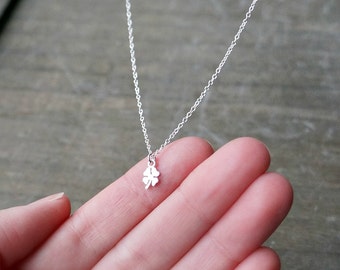 May include: A delicate silver necklace featuring a small four-leaf clover pendant. The pendant is a detailed, symmetrical design, suspended from a fine chain. The necklace is shown against a neutral background.