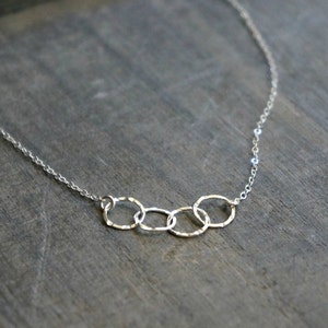May include: A silver necklace with a delicate chain and a pendant of four interconnected circles.