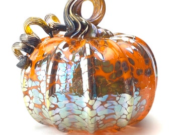 May include: A glass pumpkin ornament with an iridescent finish and a brown swirl stem. The pumpkin is orange with a white and blue iridescent pattern.