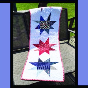 May include: A white Crazy Stars quilt with three large star designs in red and blue. The stars are made of various patterned fabrics. The quilt has a pink border and the text "Crazy Stars" is at the top.