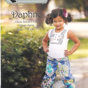 May include: A sewing pattern for a girl's "Daphne" knickers with a floral print. The pattern includes sizes 2T-10 years. The image shows a young girl wearing the finished knickers.