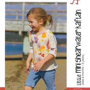 May include: A girl wearing a floral print kaftan and denim shorts. The image is from a sewing pattern book titled "Little Mini Shearwater Kaftan" with the text "make it perfect" and "modern, fresh and funky Sewing Patterns".