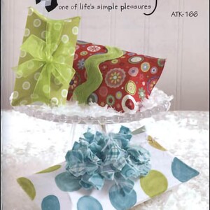 May include: Three gift boxes wrapped in different patterned paper. The boxes are stacked on a clear cake stand. The top box is green with white polka dots and a green bow. The middle box is red with white and green polka dots. The bottom box is white with blue and green polka dots and a blue bow. The text "POPOVERS" is printed in black at the bottom of the image. The text "Atkinson Designs one of life's simple pleasures ATK-166" is printed at the top of the image.