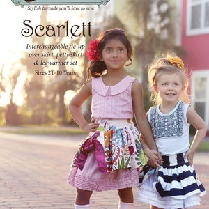 May include: Two girls wearing matching pink and white tops and colorful skirts. The girl on the left is wearing pink and white polka dot leg warmers and pink shoes. The girl on the right is wearing black and white striped leg warmers and yellow shoes. The girls are holding hands and smiling. The image is titled "Scarlett" and says "Interchangeable tie-up over skirt, petti-skirt & legwarmer set. Sizes 2T-10 Years."