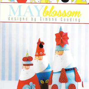 May include: Three felt Christmas ornaments in the shape of Santa Claus. The ornaments are red, blue, and white with a variety of details, including a red flower, a ladybug, and a blue bird. The ornaments are titled "Jumbleberry Santas" and are part of the "May Blossom" designs by Simone Gooding.