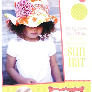 May include: A young girl wearing a white shirt and a colorful sun hat with a floral print. The hat has a large brim and a pink flower on the side. The text on the image reads "Sally Sells Sea Shells By The Seashore Sun Hat" and "Izzy & Ivy designs."