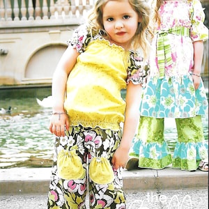 May include: Two young girls wearing colorful floral print dresses with ruffles. The girl on the left is wearing a yellow top with a brown and green floral print skirt. The girl on the right is wearing a pink and green floral print dress with a green and white striped sash. The image includes the text "Pink Fig Patterns".