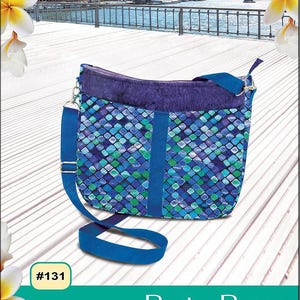 May include: A crossbody bag with a blue and green geometric pattern. The bag has a blue strap and a purple top. The text "Pink Sand Beach Designs" and "Paris Purse" are visible. The bag has an easy zipper top and lots of pockets.