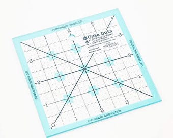 May include: A square, light blue quilting ruler with black grid lines and measurements. The ruler has the text "Cute Cuts 4 1/2" Trim-it Ruler" and "1/4" seam allowance" printed on it. The ruler is designed for trimming fabric.