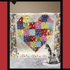 May include: A handmade quilt with a heart-shaped design made of colorful patchwork squares. The quilt features the word "Heartbeat" at the top and a small rocking horse in front. The quilt is made by Tricia Lynn Maloney.