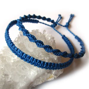 May include: Two blue braided friendship bracelets on a white crystal background.