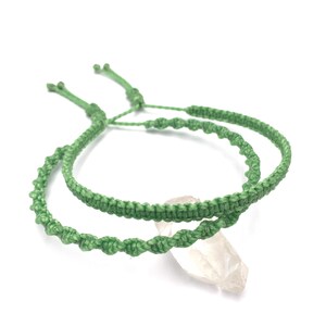 Peut inclure: Deux bracelets macramé verts avec fermetures réglables, fabriqués à partir de cordon noué, sont présentés sur fond blanc. Les bracelets présentent un motif en spirale. Un cristal clair est visible en dessous.
