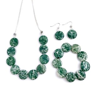 May include: A jewelry set featuring a necklace, bracelet, and earrings. The necklace and bracelet are composed of round, green and white speckled beads. The earrings have matching green and white speckled beads. The jewelry is set against a white background.