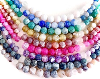 May include: A collection of colorful, round beads arranged in a semi-circular pattern. The beads display a range of colors, including pink, purple, blue, green, yellow, and white. Each bead has a unique, crackled surface texture, creating a visually appealing display.