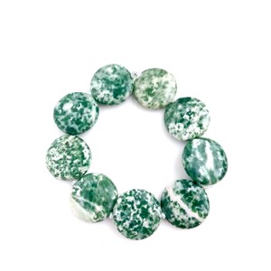 May include: A circular arrangement of green and white speckled gemstone beads. The beads are flat, round, and approximately 1 inch in diameter. The beads are strung together, forming a complete circle against a white background.
