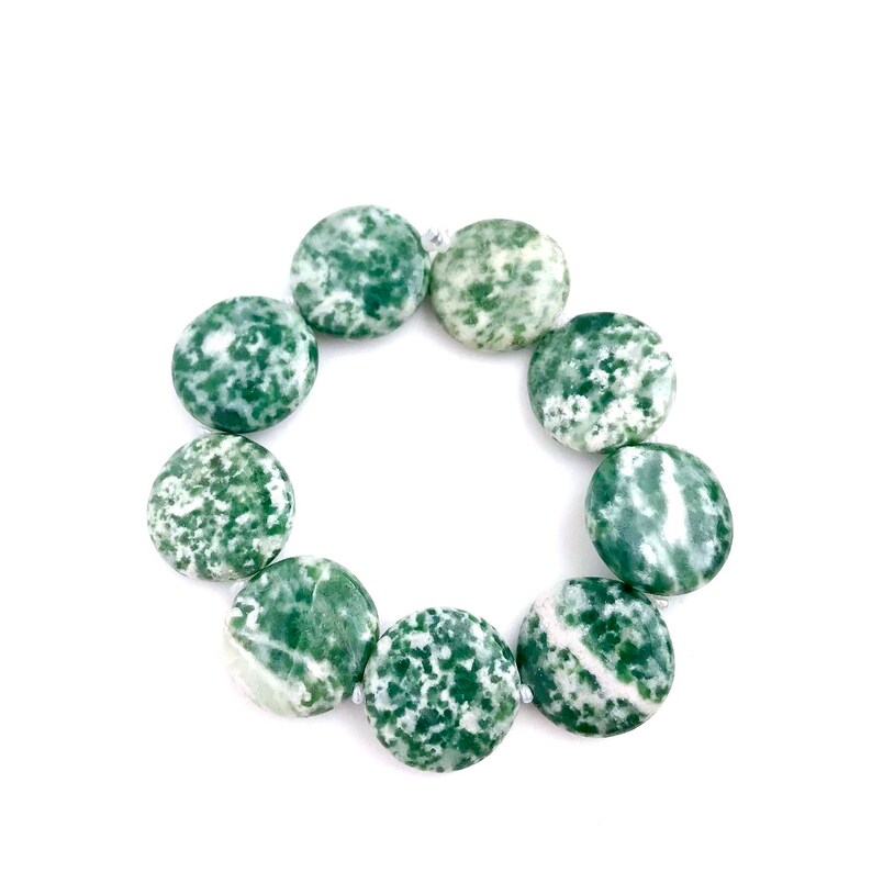 May include: A circular arrangement of green and white speckled gemstone beads. The beads are flat, round, and approximately 1 inch in diameter. The beads are strung together, forming a complete circle against a white background.