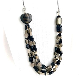 May include: A multi-strand necklace with black and gray beads. The necklace has a silver chain and a large, dark gray bead at the top.