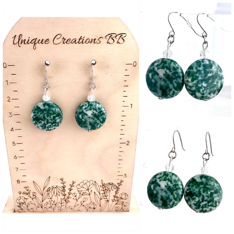 May include: Green and white speckled stone earrings with silver-colored hooks and a small clear bead accent. The earrings are displayed on a wooden stand with the text "Unique Creations BB". Additional earrings are shown in the image.