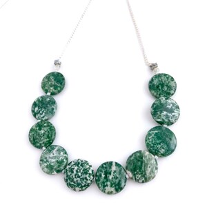 May include: A necklace featuring large, round, green and white speckled beads. The beads are strung on a delicate silver chain. The necklace is displayed against a white background, highlighting the natural stone beads.