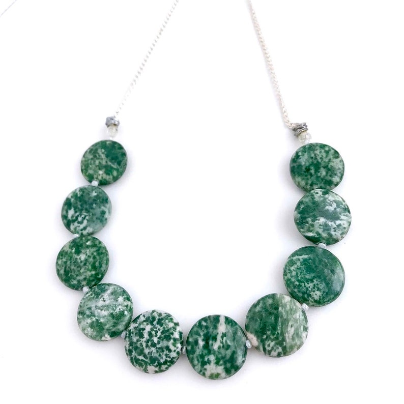 May include: A necklace featuring large, round, green and white speckled beads. The beads are strung on a delicate silver chain. The necklace is displayed against a white background, highlighting the natural stone beads.