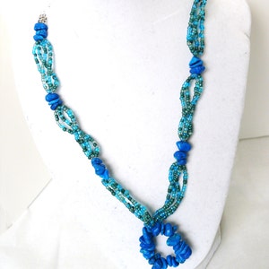 May include: A multi-strand necklace with blue and green beads. The necklace has a large pendant made of blue stones in the shape of a circle.