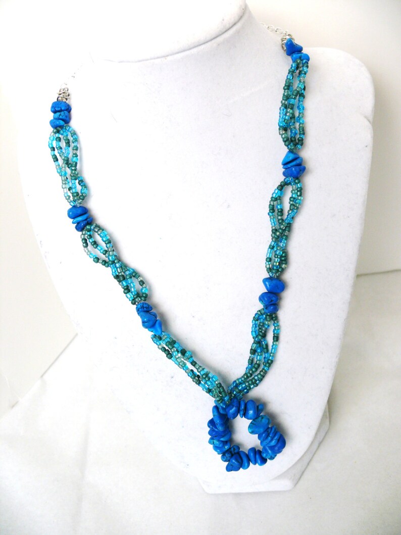 May include: A multi-strand necklace with blue and green beads. The necklace has a large pendant made of blue stones in the shape of a circle.
