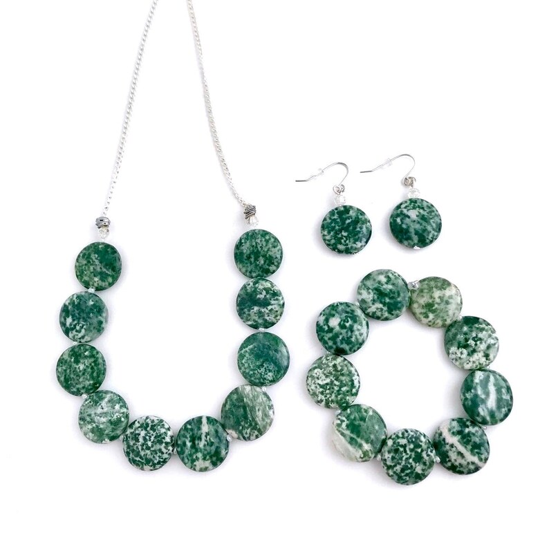 May include: A jewelry set featuring a necklace, bracelet, and earrings. The necklace and bracelet are composed of round, green and white speckled beads. The earrings have matching green and white speckled beads. The jewelry is set against a white background.