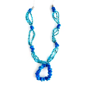 May include: A blue and turquoise beaded necklace with a large blue bead pendant. The necklace is made of multiple strands of beads and has a simple design.