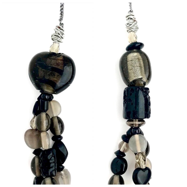 May include: A multi-strand necklace with black, gray, and clear glass beads. The necklace features a heart-shaped bead at the top and a variety of other shapes and sizes throughout.