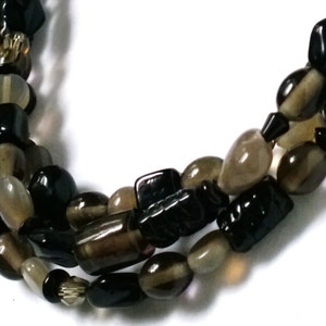 May include: A multi-strand necklace made of black and brown gemstone beads. The beads are various shapes and sizes, including oval, round, and rectangular.