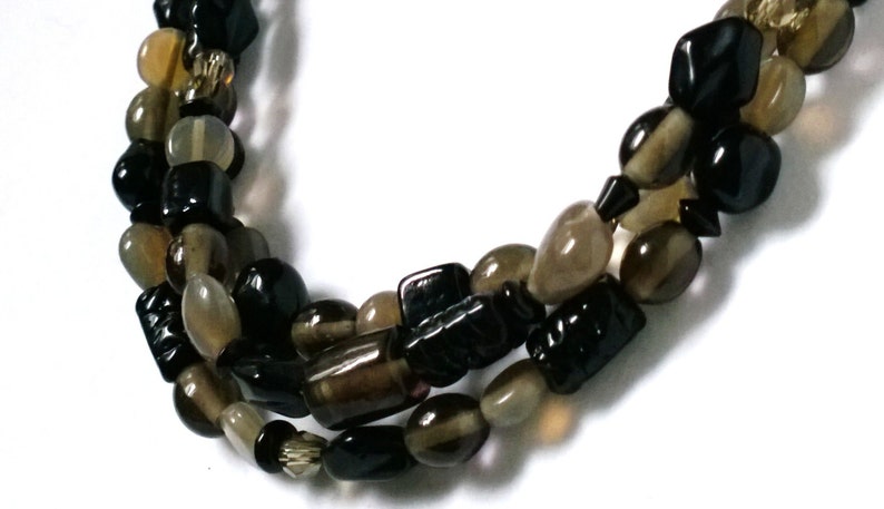 May include: A multi-strand necklace made of black and brown gemstone beads. The beads are various shapes and sizes, including oval, round, and rectangular.