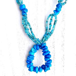 May include: A turquoise blue necklace with multiple strands of smaller blue beads. The necklace has a large turquoise blue pendant in the shape of a circle.
