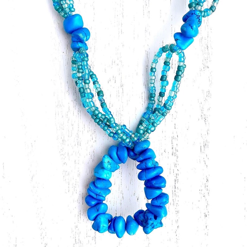 May include: A turquoise blue necklace with multiple strands of smaller blue beads. The necklace has a large turquoise blue pendant in the shape of a circle.