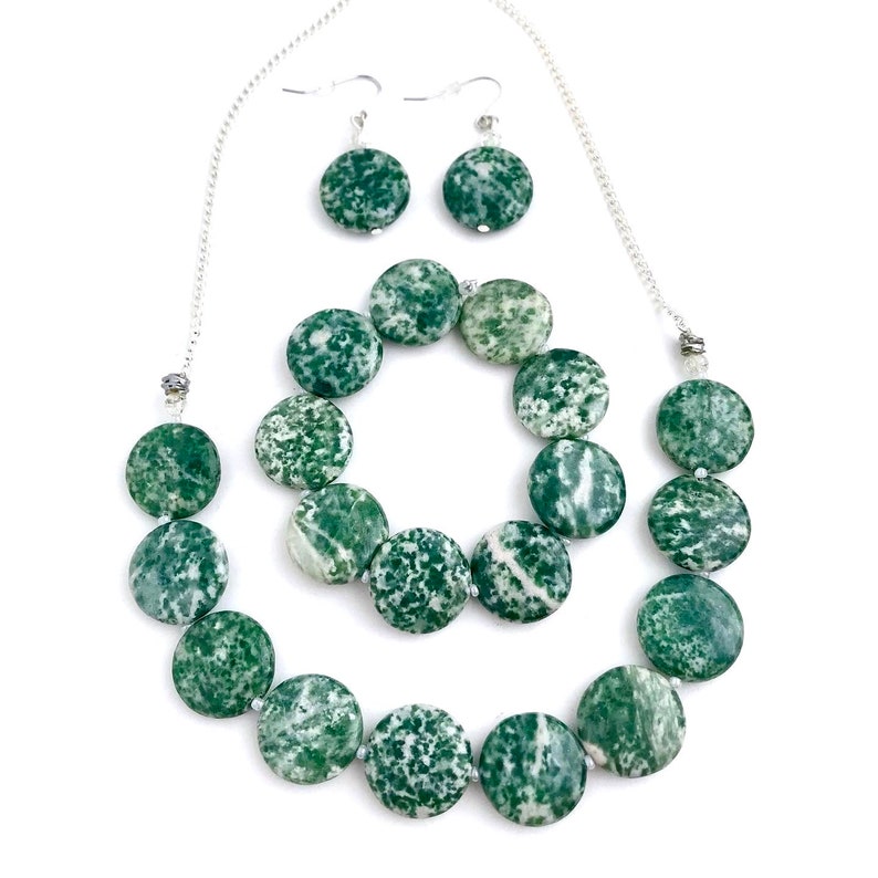 May include: A jewelry set featuring a necklace and matching earrings. The necklace and earrings are made of round, green and white speckled beads. The necklace has a silver chain, and the earrings have silver hooks.