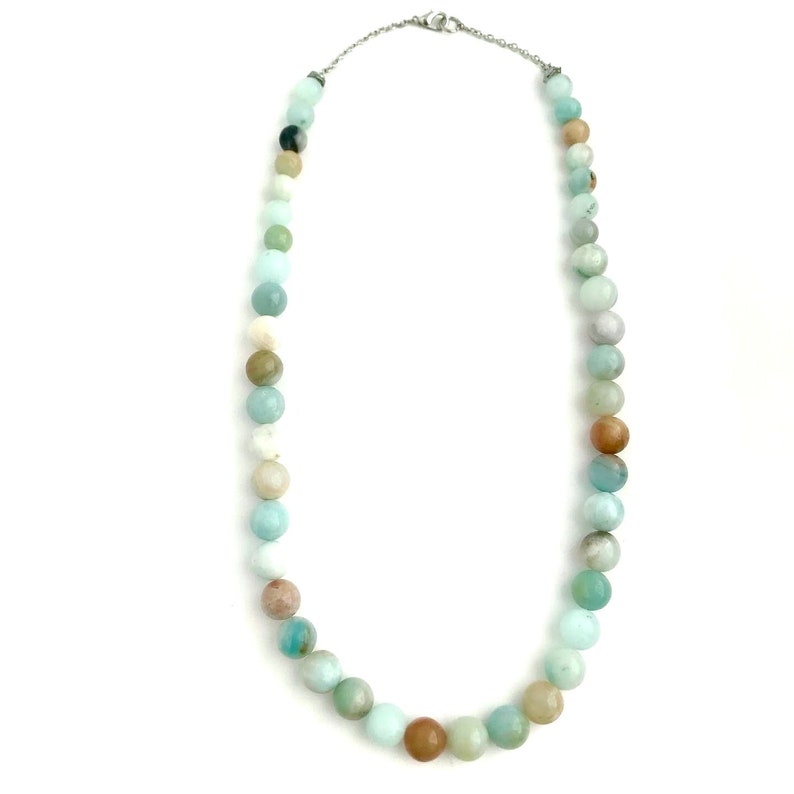 May include: A long necklace made of light blue, green, and brown beads. The necklace is made of round beads and has a silver clasp.