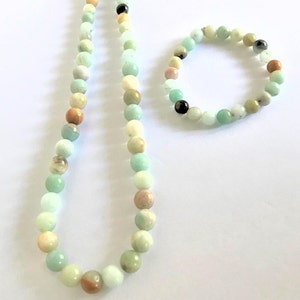May include: A set of green, brown, and white gemstone beads, one necklace and one bracelet. The necklace is longer and has a silver clasp. The bracelet is shorter and has no clasp.