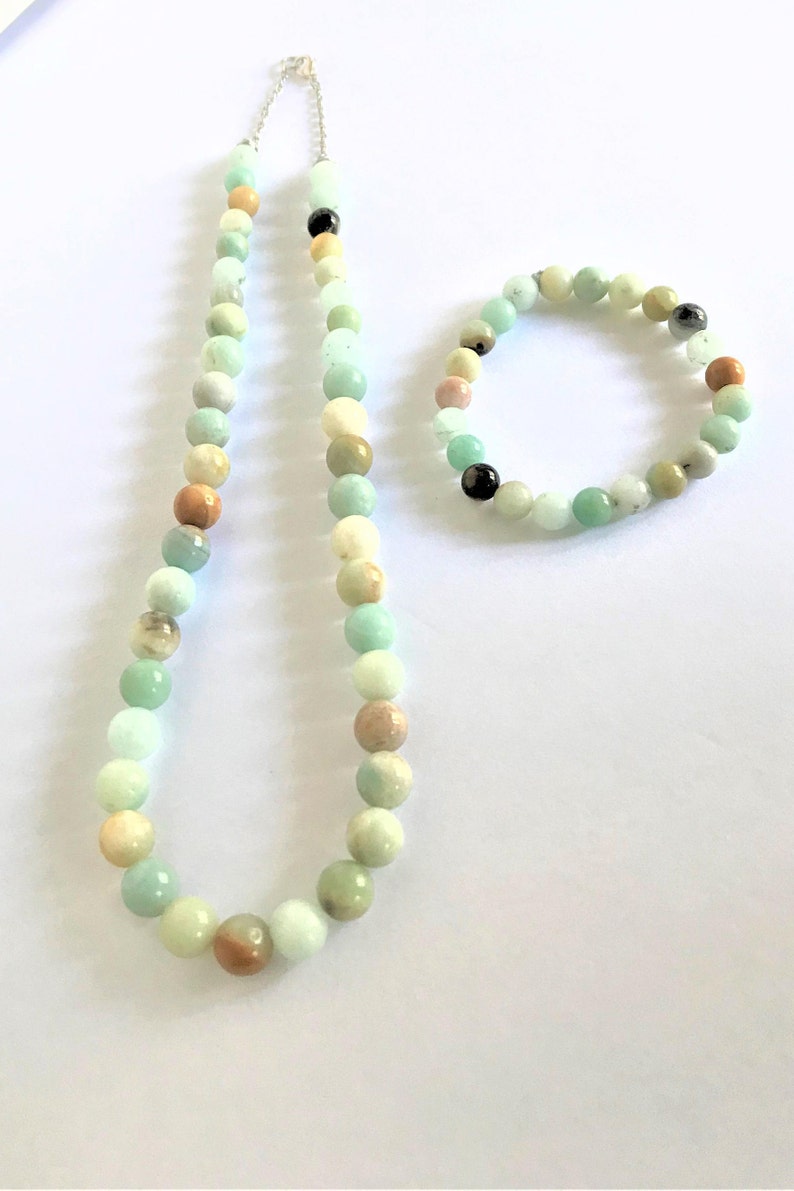 May include: A set of green, brown, and white gemstone beads, one necklace and one bracelet. The necklace is longer and has a silver clasp. The bracelet is shorter and has no clasp.