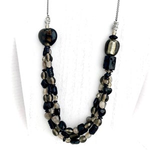 May include: A multi-strand necklace with black, brown, and clear glass beads. The necklace features a heart-shaped bead and a square bead.