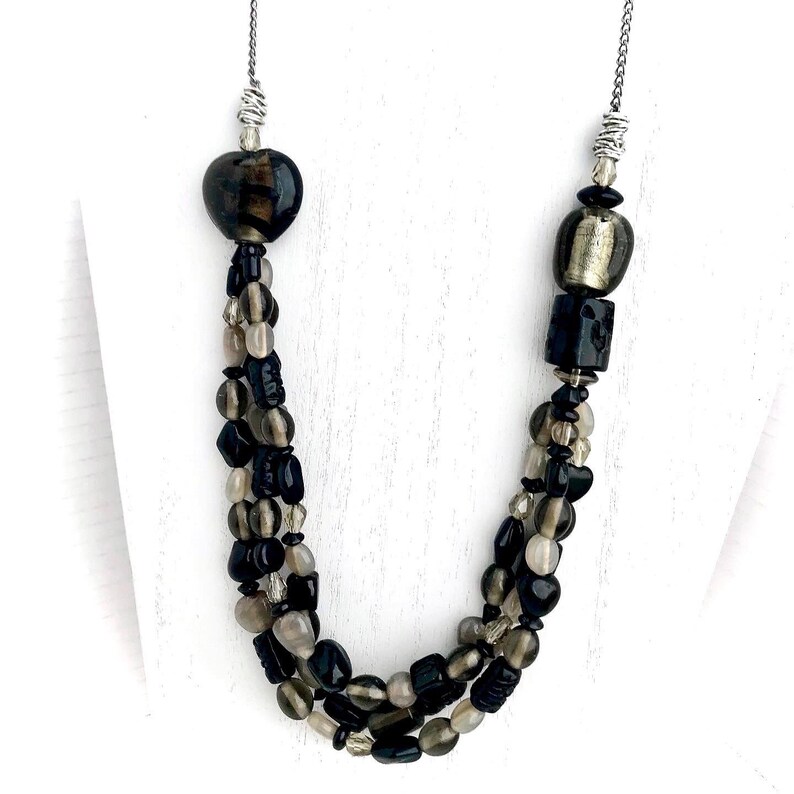 May include: A multi-strand necklace with black, brown, and clear glass beads. The necklace features a heart-shaped bead and a square bead.