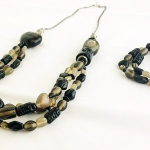 May include: A three-strand necklace and matching bracelet set with black and brown beads. The necklace has a heart-shaped pendant and the bracelet is a single strand.
