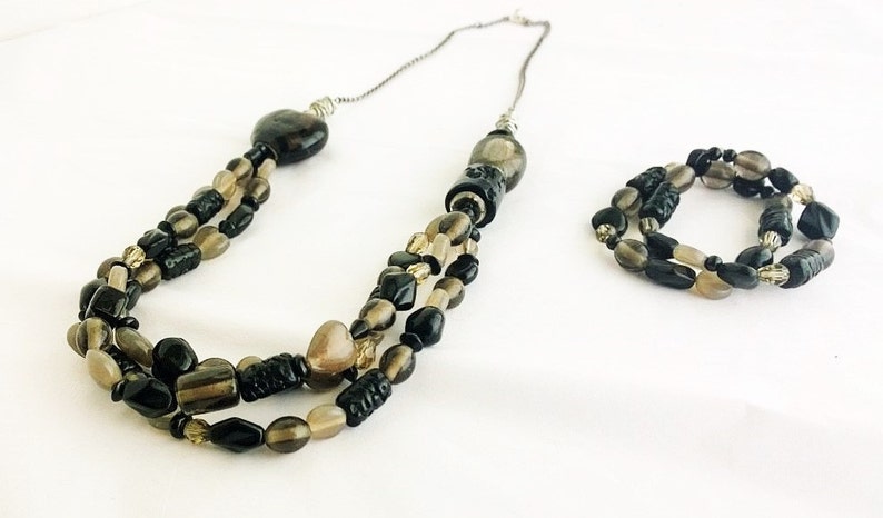 May include: A three-strand necklace and matching bracelet set with black and brown beads. The necklace has a heart-shaped pendant and the bracelet is a single strand.